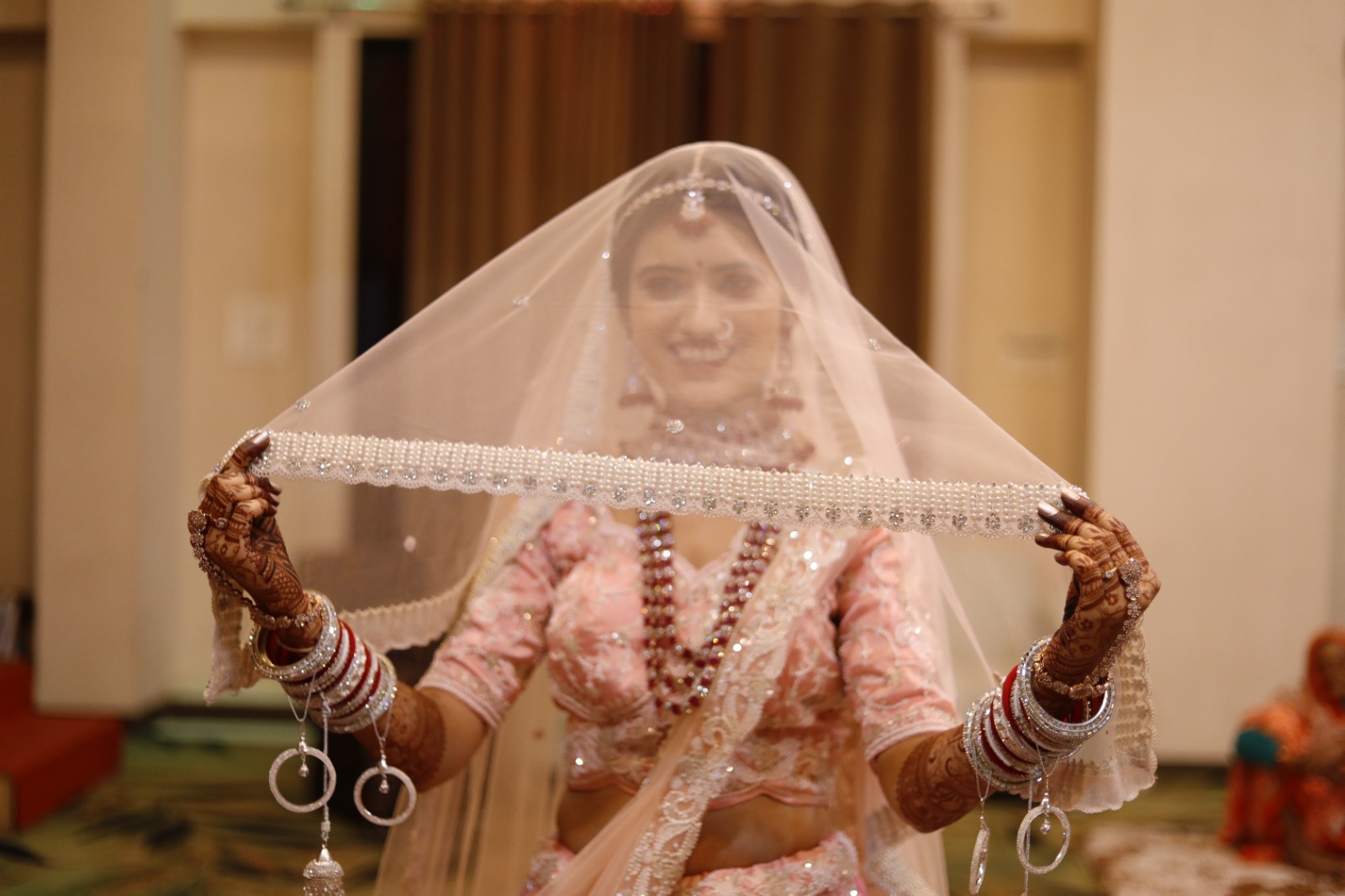Bride smiling behind her veil with mehndi-covered hands